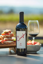 Photo of a bottle of 2023 HALL Craig's Cabernet Sauvignon on a picnic table with a platter of sandwiches, a summer salad, and glass of red wine in the background.