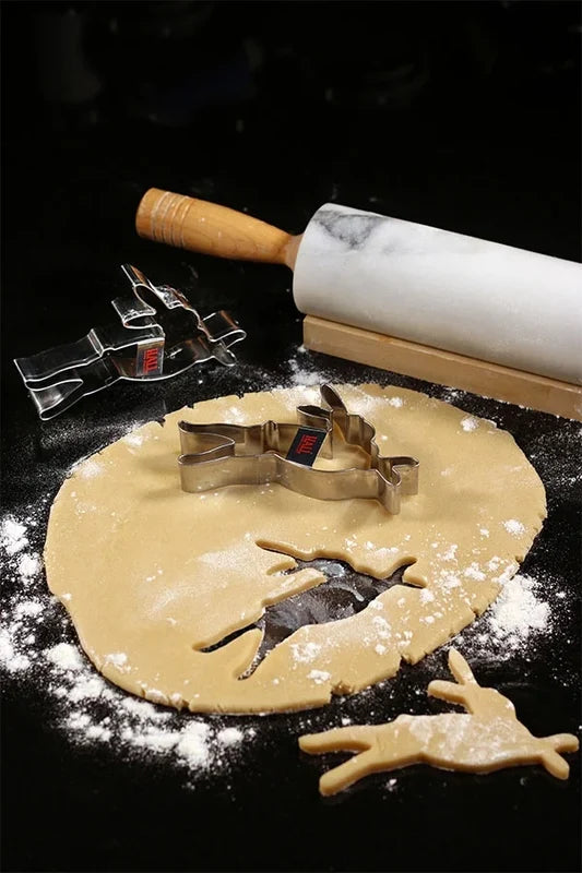 Rolling pin, HALL bunny foo foo cookie cutters, and dough with the bunny shape cookies cut out on a dark surface